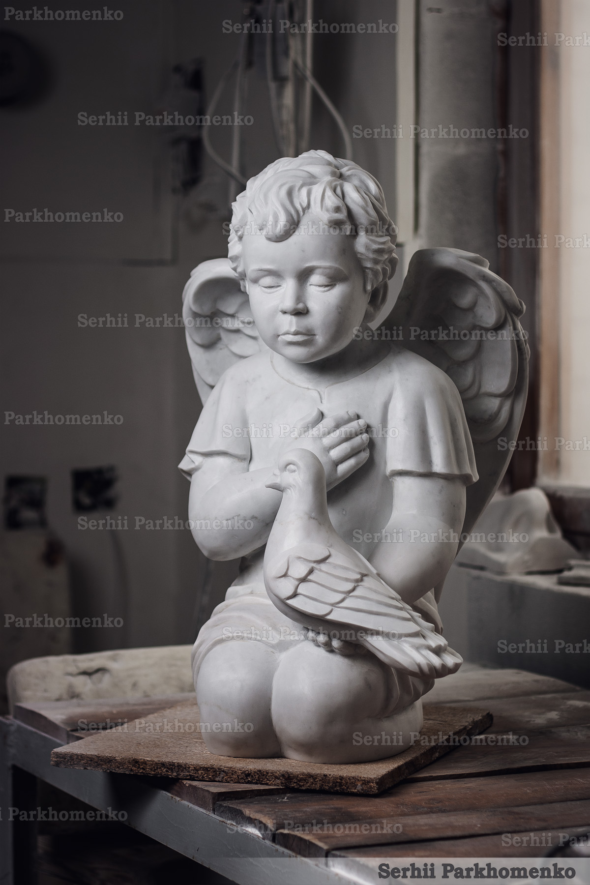 Kneeling marble angel statue holding a dove with a smooth honed finish by Serhii Parkhomenko's Stone Architecture & Design Studio
