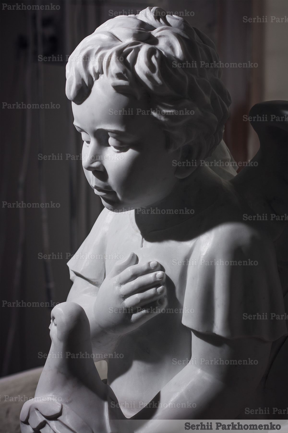 Close-up detailing the serene face of a hand-carved marble angel sculpture under dramatic lighting